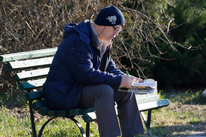 A man playing crossword outside. He has a nice cap